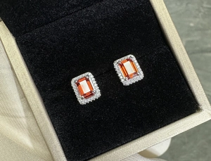 Close-up of emerald cut ruby silver earrings with halo diamonds in a jewelry box