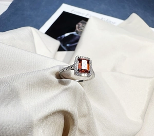 Macro view of a 925 silver ring with a rectangle emerald cut orange gemstone and halo diamonds