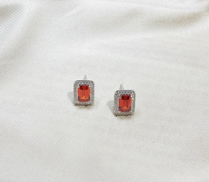 Detailed close-up of emerald-cut ruby halo stud earrings on elegant white satin background