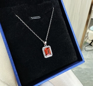 Detail of emerald cut orange-red ruby necklace in a luxury blue jewelry box