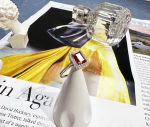 Detailed halo setting of rectangle emerald cut red ruby ring on white display stand