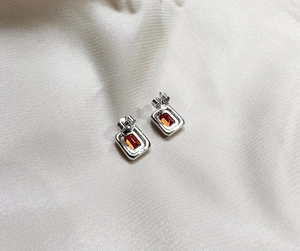 Detail view of emerald cut orange ruby studs on 925 sterling silver set on silk fabric