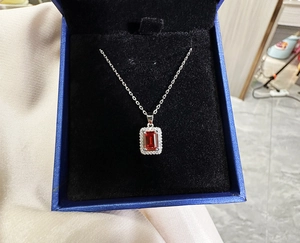 Close-up of emerald cut ruby necklace in a blue jewelry gift box with silver chain
