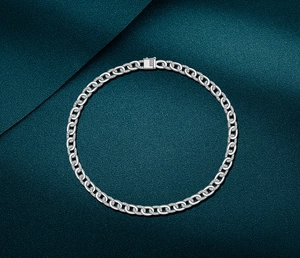 Macro detail of silver Cuban link necklace with pavé diamonds on dark green satin fabric