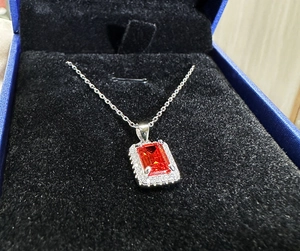 Macro detail of rectangle cut ruby pendant with diamond halo on silver chain