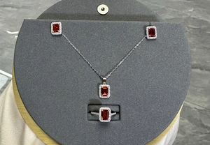 Three-piece silver jewelry set featuring emerald-cut red gemstones and micro-pave halo details