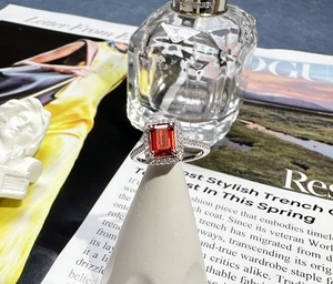 Detail of emerald cut red ruby ring with halo diamonds on a white cone stand