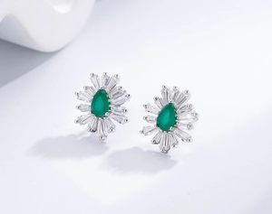 Macro detail of 925 silver stud earrings with teardrop emerald and baguette zirconia