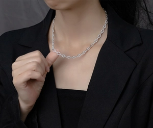 Close-up of a silver Cuban link necklace with micro-pave diamonds on a model in a black suit
