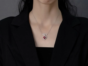Détail du collier pendentif cœur rouge avec nœud porté sur un blazer noir chic