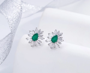Macro shot of 925 silver stud earrings with pear-cut emerald and sunburst cubic zirconia