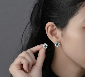 Macro detail of daisy emerald pear-cut earrings with white zircon petals on ear
