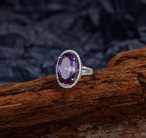 Détail d'une bague avec pierre violette ovale et halo de diamants sur fond d'écorce