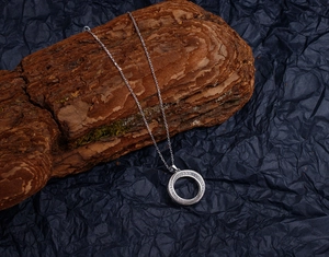 Detail of silver S925 Möbius necklace pendant with pavé cubic zirconia on wooden bark