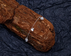 Détail du bracelet cœur en argent avec breloques en zircone sur texture bois rustique