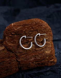 Detailed view of silver hoop earrings with double-row crystals on rustic bark texture