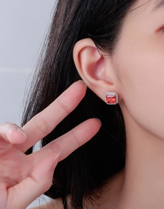 Gros plan de boucles d'oreilles en rubis orange-rouge avec halo de diamants sur mannequin