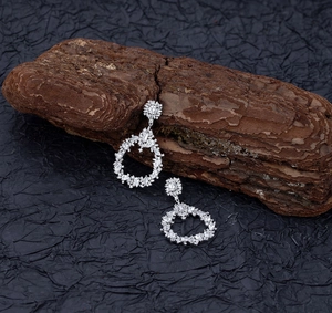 Macro detail of teardrop hollow flower earrings with marquise crystals on dark wood texture