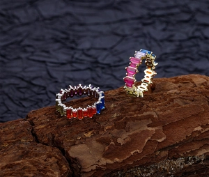 Detail of colorful baguette-cut rainbow zircon rings in silver and gold on tree bark