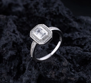 Macro shot of an emerald cut silver ring with halo diamonds on dark volcanic rock