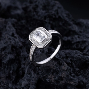 Emerald-cut halo ring with pave-set diamond band on a black volcanic stone background