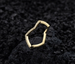 Macro view of V-shaped gold ring with pavé-set clear zircons on black volcanic rock