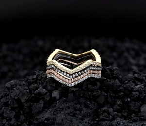 Macro detail of V-shaped stacking rings in four metallic tones on black volcanic rock
