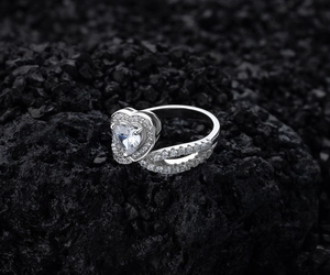 Macro d'une bague diamant cœur sur roche noire montrant l'anneau croisé serti de pavé