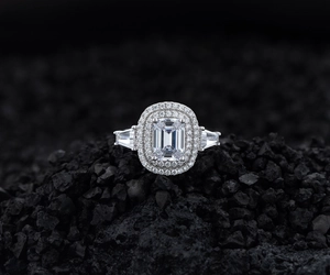 Macro shot of emerald cut ring with double halo and trapezoid side stones on black rock