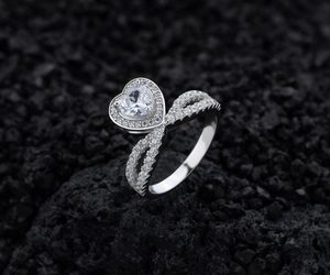 Gros plan d'une bague en argent avec diamant coeur sur fond de pierre volcanique