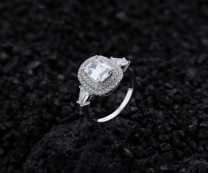 Close-up of S925 silver halo ring with emerald-cut main stone on black volcanic stone