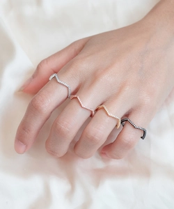 Close-up of four stacked wavy pavé rings in silver, gold, rose gold, and black
