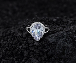 Macro shot of S925 silver pear-cut diamond ring with halo setting on a black rock surface