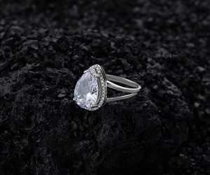 Macro detail of pear-cut halo diamond ring with split-shank design on dark rock