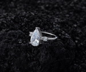 Macro detail of pear cut diamond ring with pavé diamonds on a black volcanic stone