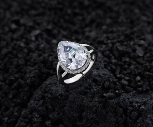 Macro shot of S925 sterling silver pear-cut diamond halo ring on black volcanic stone
