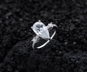 Detailed view of pear-cut diamond sterling silver ring on textured black volcanic rock