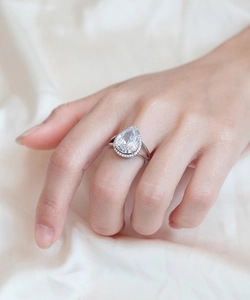 Macro detail of pear-shaped halo engagement ring on silk background