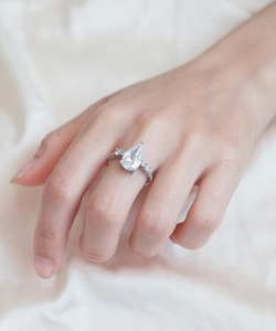 Detailed view of a pear-shaped diamond sterling silver ring on a soft silk background