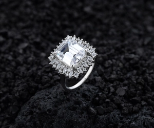 Macro view of emerald-cut center stone with marquise halo on black volcanic rock
