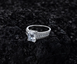 Gros plan d'une bague en argent 925 avec diamant taille émeraude sur roche volcanique noire