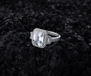 Macro detail of emerald cut zircon halo ring on black volcanic stone, 925 silver jewelry