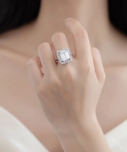 Macro view of emerald cut gemstone ring with sparkling diamond halo on finger