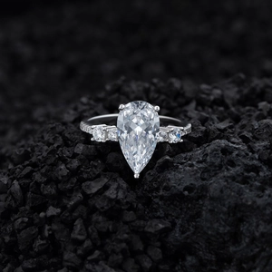 Pear cut teardrop diamond ring in sterling silver with side stones on dark volcanic rock