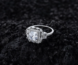Détail macro d'une bague halo carrée en argent 925 sur une roche volcanique noire mate