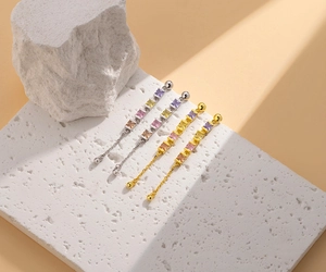 Detail of S925 silver fringe earrings with colorful square zircons on stone background
