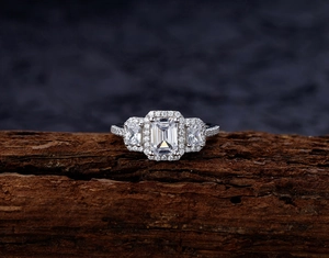 Macro detail of silver emerald cut three-stone ring with halo design on a rustic wood base