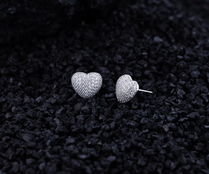 Close-up of pavé heart earrings with white zircons on a textured black mineral background