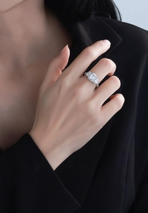 Detailed view of an emerald cut silver ring with side stones on a model's hand