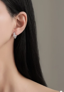 Detail view of silver S925 stud earrings with triple wave rows on a model's ear